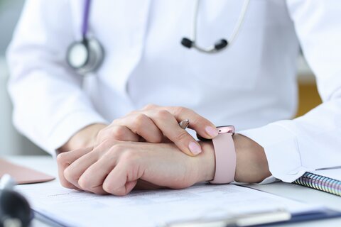 Ärztin hält Stift und schaut auf ihre Armbanduhr