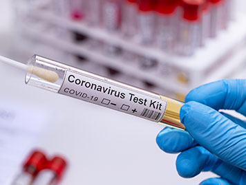 Abstrichstab wird in ein Coronavirus Teströhrchen geschoben. Im Hintergrund sind mehrere aufgestellte Teströhrchen zu sehen.