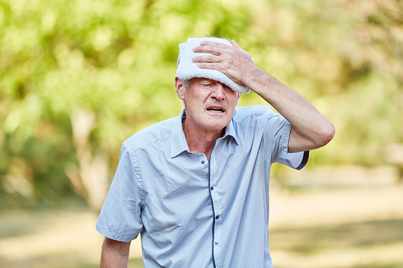 Älterer Mann hält sich ein Tuch an die Stirn.