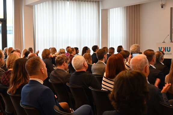 Publikum der Herbsttagung in einem Tagungsraum von hinten fotografiert.