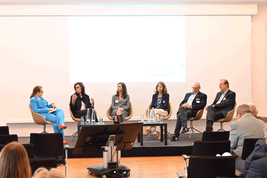 Mehrere Personen sitzen in einem Veranstaltungsraum vor Publikum auf einem Podium und diskutieren.