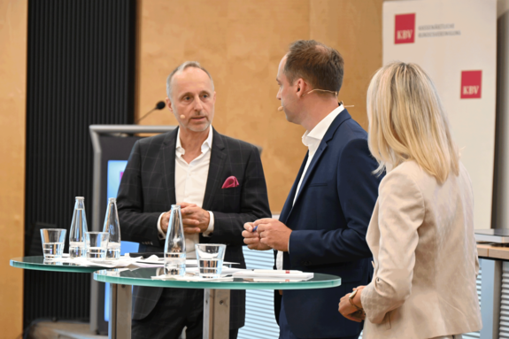Dr. Stephan Hofmeister, Thomas Trappe und Stefanie Stoff-Ahnis stehen an einem Rednerpult in einem Konferenzraum.