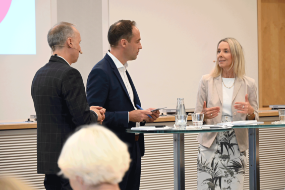 Dr. Stephan Hofmeister, Thomas Trappe und Stefanie Stoff-Ahnis stehen an einem Rednerpult in einem Konferenzraum.