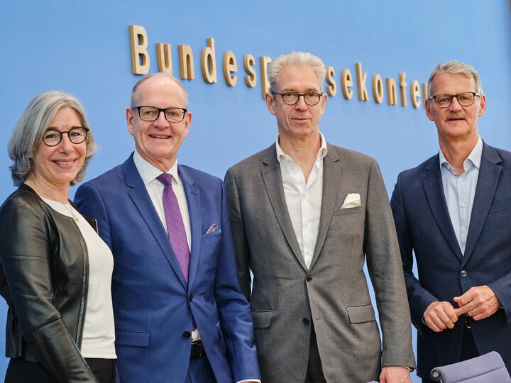 Vier Personen stehen im Saal der Bundespressekonferenz und gucken in die Kamera.