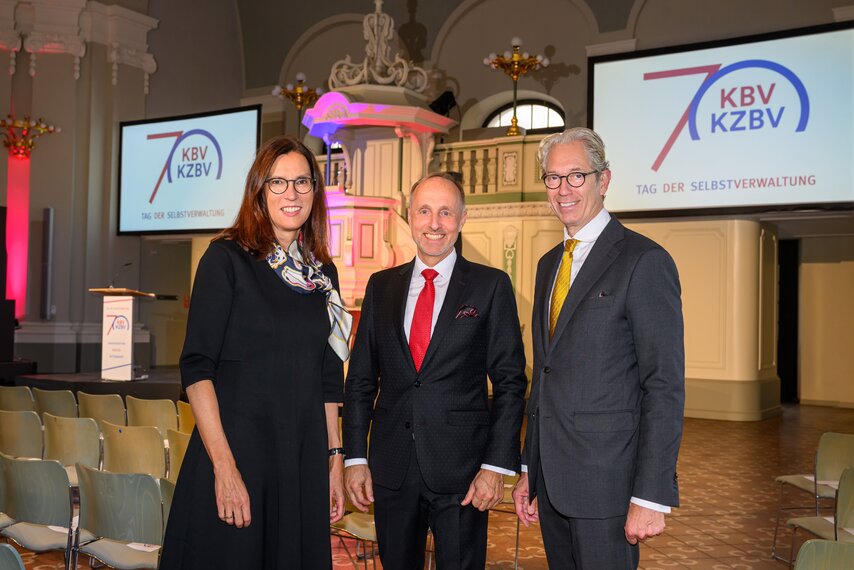 Dr. Sibylle Steiner, Dr. Stephan Hofmeister und Dr. Andreas Gassen stehen in einem Saal und lächeln in die Kamera.