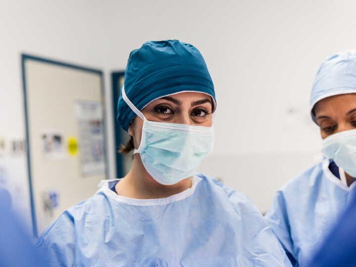 Ärztin in blauer OP-Kleidung schaut in die Kamera