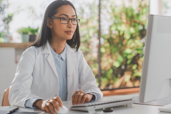 Ärztin sitzt am Computer und guckt auf den Bildschirm