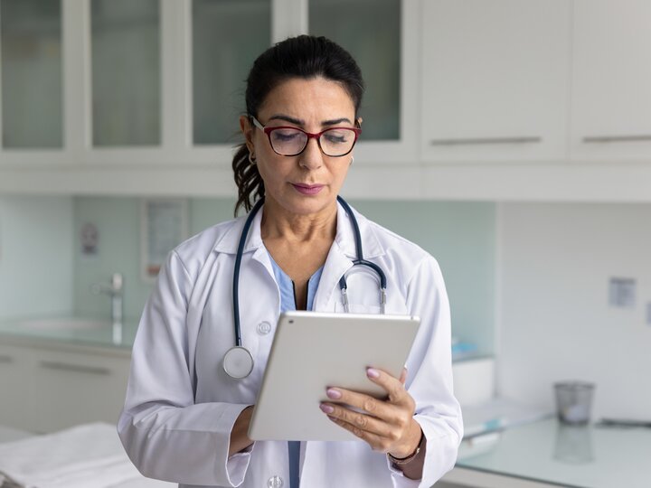 Eine Ärztin guckt auf ein Tablet, das sie in der Hand hält. 