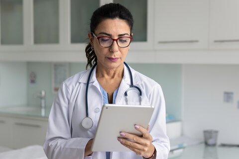 Eine Ärztin guckt auf ein Tablet, das sie in der Hand hält. 