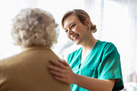 Eine freundliche Krankenschwester unterstützt eine ältere Dame 