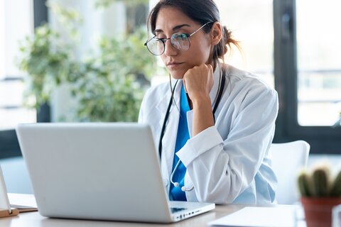 Eine Ärztin sitzt am Laptop  und guckt auf den Bildschirm.
