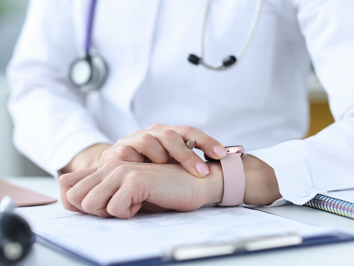 Ärztin hält Stift und schaut auf ihre Armbanduhr