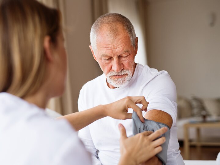 Medizinische Assistentin misst Blutdruck bei Patienten während eines Hausbesuchs