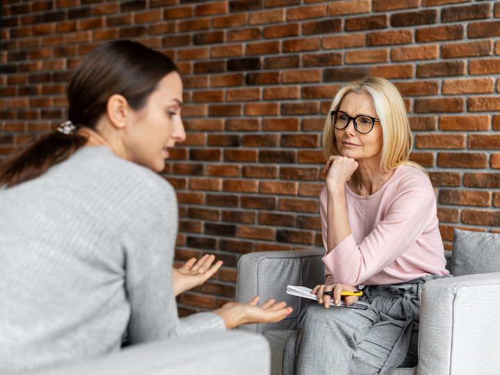 Besorgte junge Patientin sitzt auf einem bequemen Stuhl und erzählt von psychischen Problemen, aufmerksame Psychotherapeutin hört zu