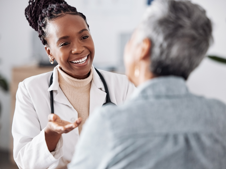 Freundlich lächelnde Ärztin berät eine Patientin. Beide sitzen sich an einem Tisch gegenüber.