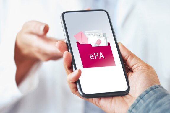 Smartphone mit Bild zur elektronischen Patientenakte wird von einer Hand in eine andere gereicht. 