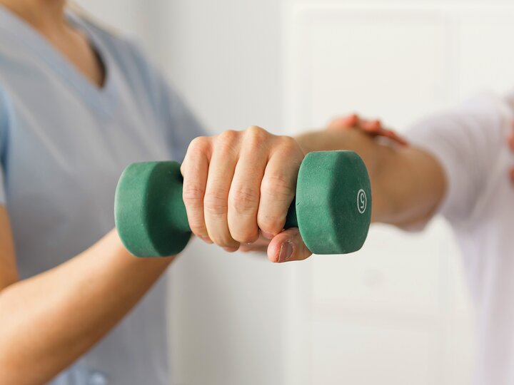 Patient hält grüne Hantel in der Hand.