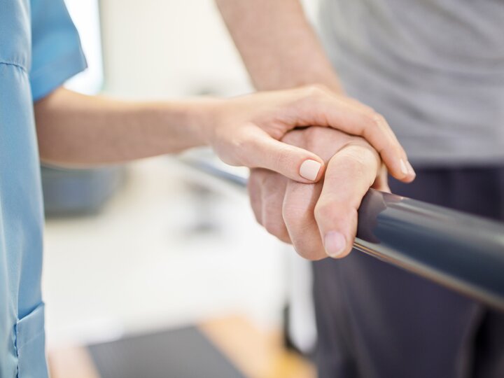Krankenschwester berührt Hand eines Rehabilitationspatienten an einem Trainingsgeländer.
