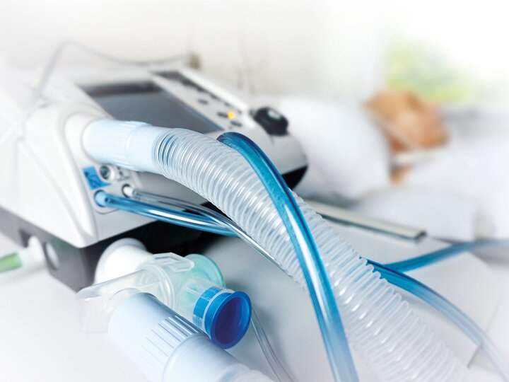 Beatmungsgerät bei der Außerklinischen Intensivpflege mit verschwommenem Patienten im Hintergrund.