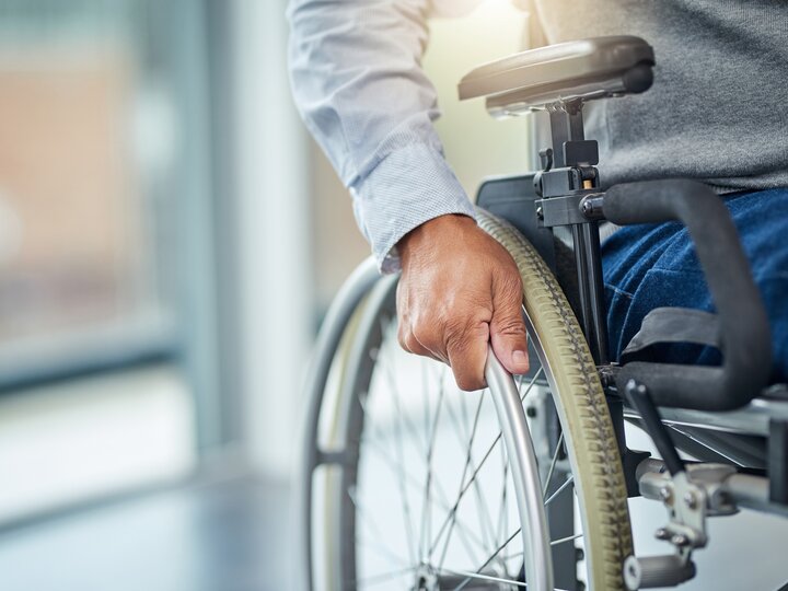 Ausschnitt eines Mannes mit Hemd, grauem Pullunder und Jeans in einem Rollstuhl.