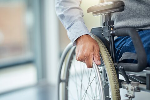 Ausschnitt eines Mannes mit Hemd, grauem Pullunder und Jeans in einem Rollstuhl.