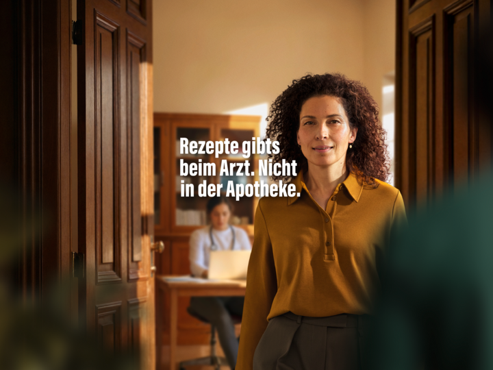 Rezepte gibts beim Arzt. Nicht in der Apotheke. Eine Frau steht in einer Arztpraxis und guckt in die Kamera.